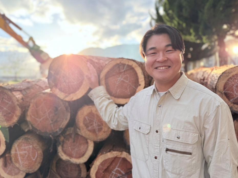 丸太の前で微笑む大川さん